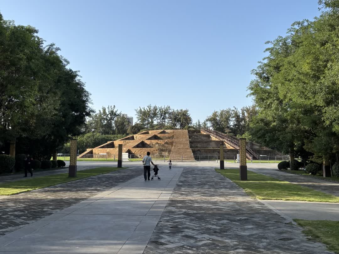 畫面以石板路為引導線,指向遠處棕色的天壇。背景是晴朗的天空和茂密的綠色樹木。有成人和兒童在石板路上散步。